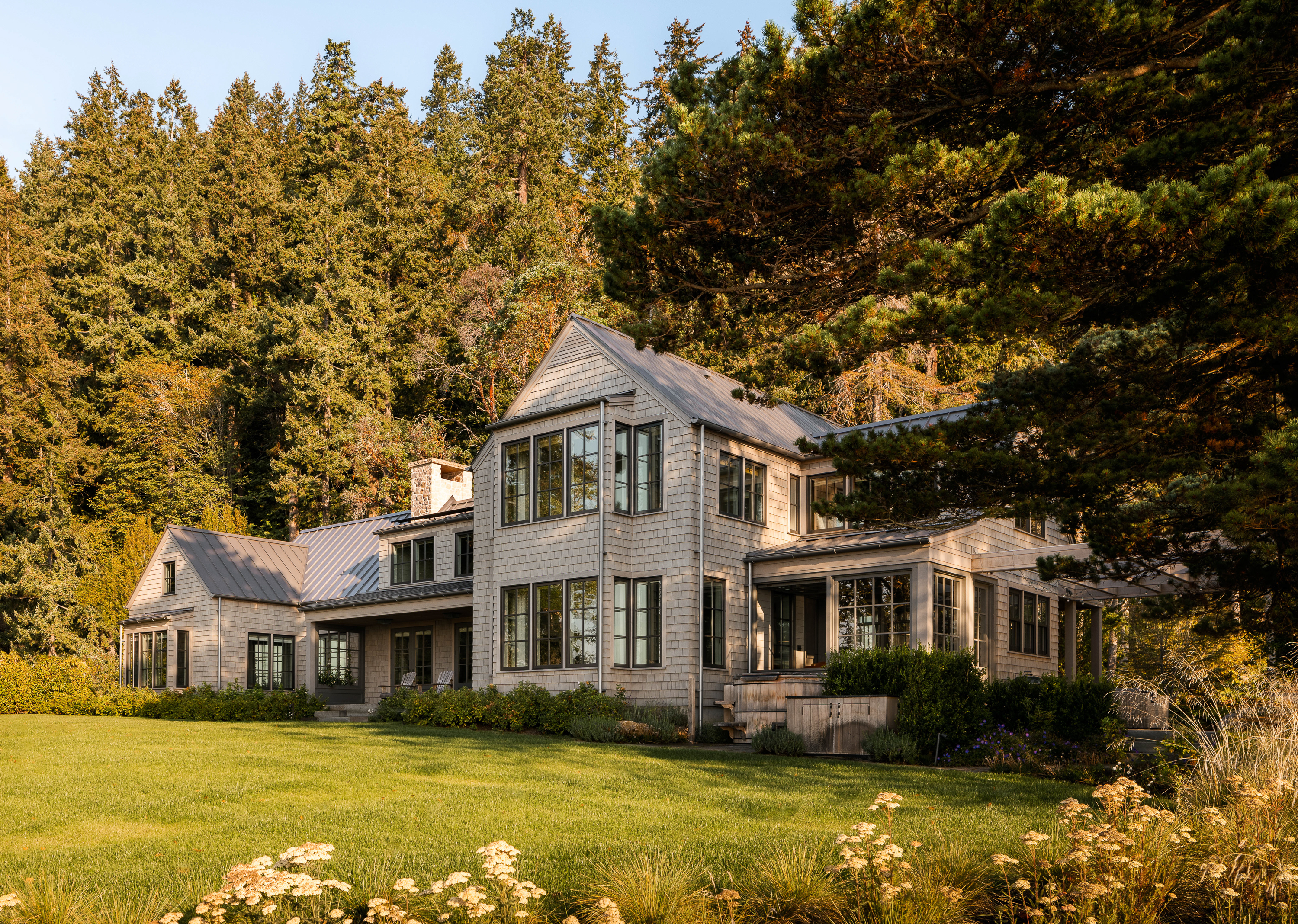 The waterside of the home features natural shingles and a metal roof, embodying a timeless architectural design that harmonizes with its waterfront setting.